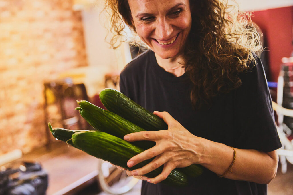 Fröhliche Mitarbeiterin bringt Salatgurken, Fotografin Julia Schwendner