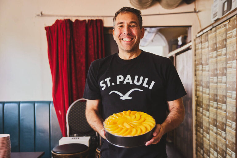 Ein fröhlicher ehrenamtlicher Mitarbeiter zeigt einen Kuchen mit Pfirsichen her, Fotografin Julia Schwendner